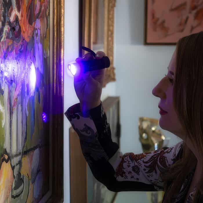 Person using a purple flashlight to inspect artwork on a wall
