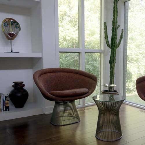 Modern brown chair and glass table in a room with large windows and a cactus plant.