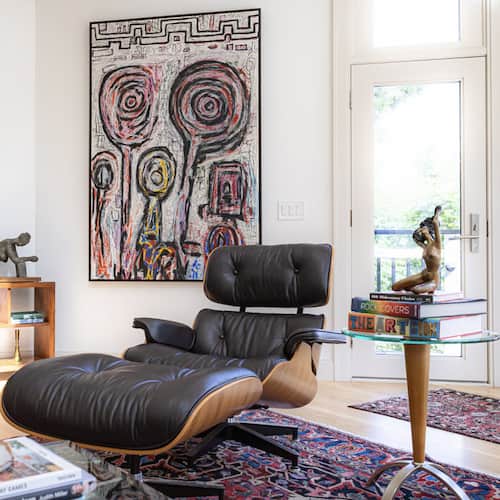 Modern living room with black leather lounge chair, colorful abstract painting, and glass table.